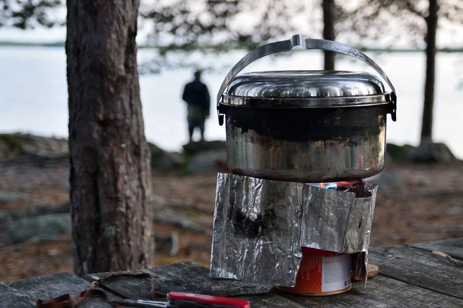 A camping stove burning beside a metal pot